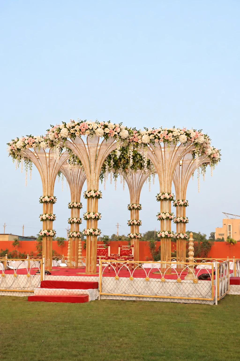 Ornate gold mandap with white and blush flowers in the open garden under clear blue skies